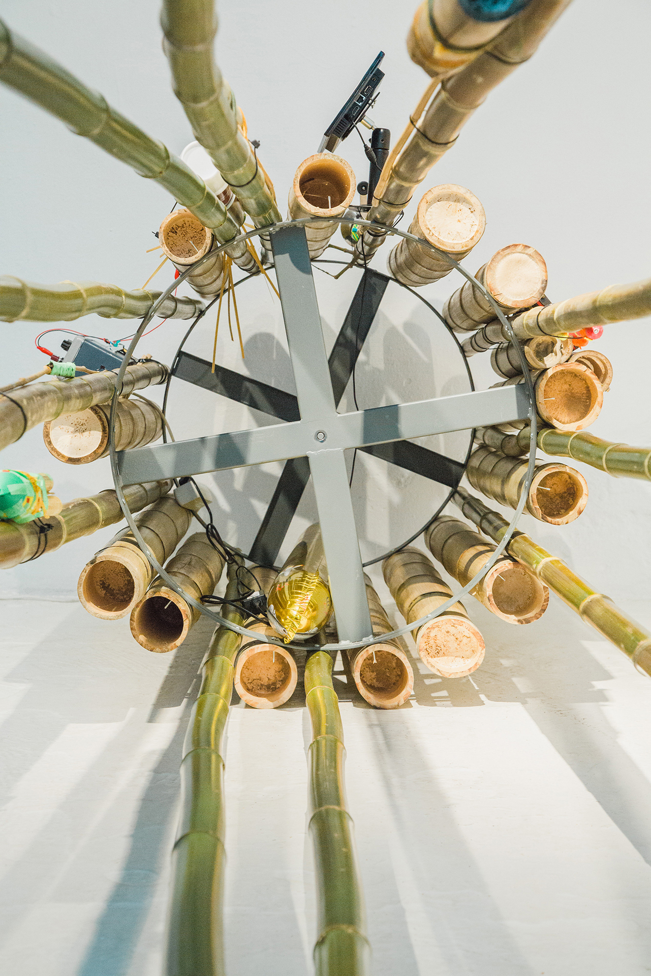 Monika Czyżyk and Torsten Zenas Burns, Geographies of a lonely Pole (Cluster) , 2020, 24 bamboo poles mounted on steel hoop rack, screws, zip ties, threads, 10” screen, 12VDC motor, bamboo cotton swabs, bamboo cutlery set, thermos, coffee grinder, green mesh, capacitors, USB connectors, trimmer, 232 chip, socket rails with flat cables, 286 x Ø 70 cm