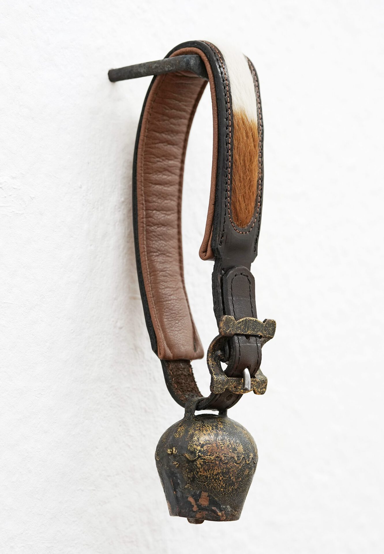 Eliza Ballesteros, DOMESTIC HECK III, 2020, antique goat bell with fur and buckle, brass, leather, fur, iron hook, 30 x 7 x 14 cm