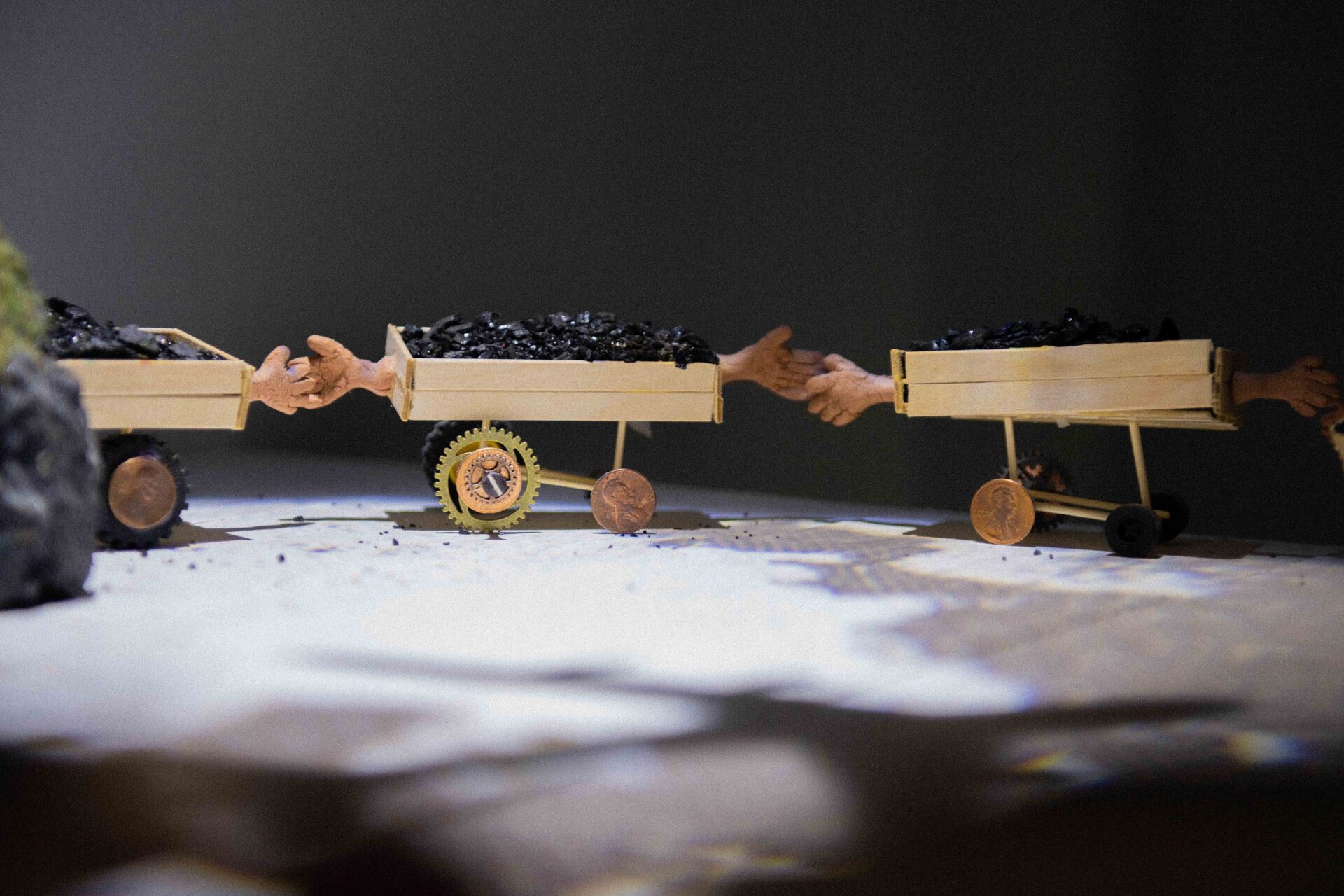 Detail shot of Community Meeting, 2020, 3'8" x 3' x 2'5", wire, coal, popsicle sticks, toothpicks, Static grass, clay, pennies, watch gears, toy wheels, office chair wheels, wood, house paint, spotlight, moon transparency
