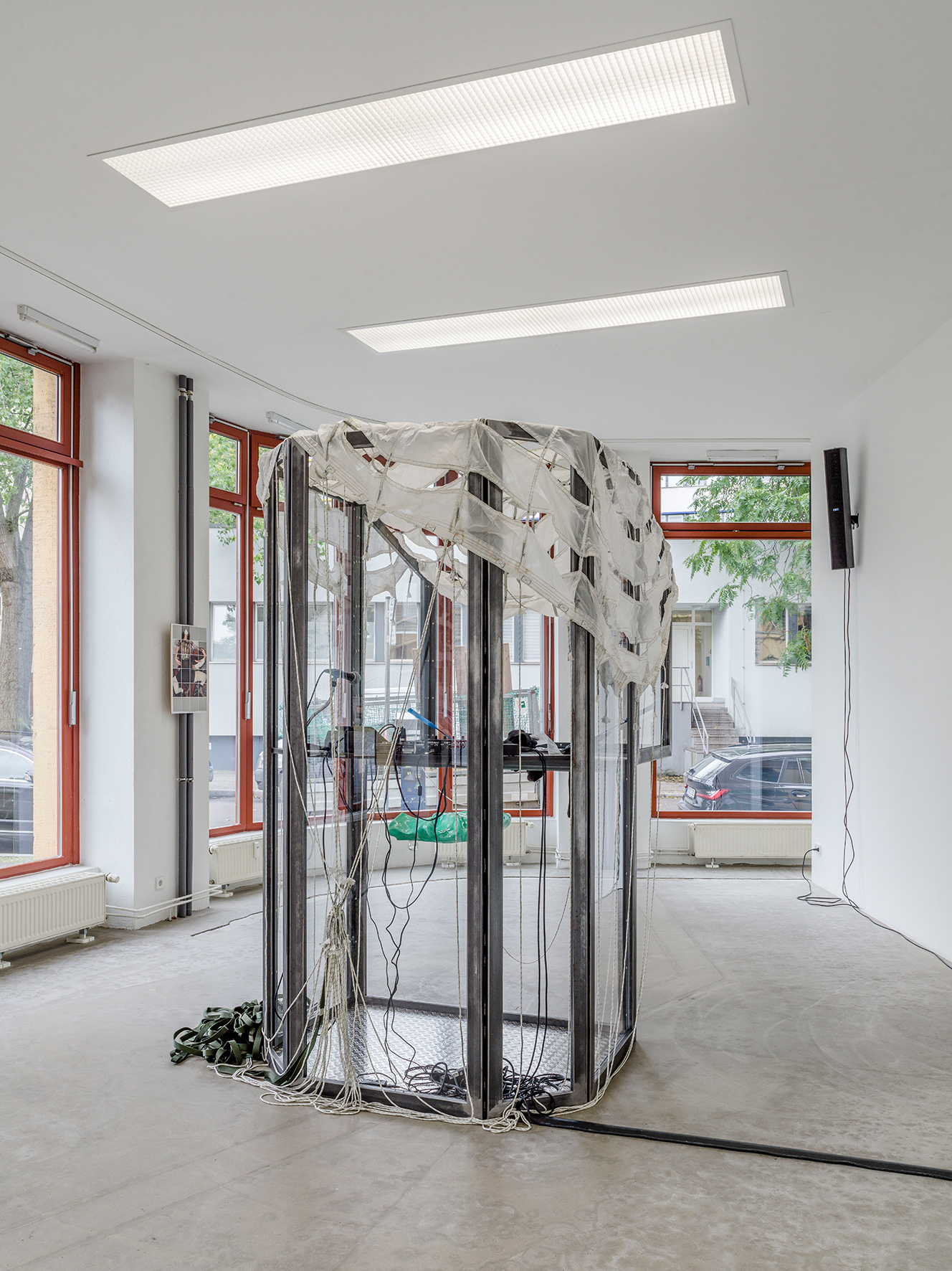 Mara Wohnhaas, “Rekommandeur I”, 2021, 2-parts, Cabin: Steel, chequer plate, polycarbonate, glass, MDF, parachute, mixing console, microphone, linear wave sampler, touch matrix mic stand-mount vocal effects processor, DJDI-box, lacquered plastic seat, lacquered rubber gloves, photo album, leather gloves with badminton racket and fishhooks, rubber gloves, texts on transparent paper, chain rings, 2 speakers, audio cable, sound 10 min (in collaboration with Simon Wallnöfer), 253 x 200 x 208,5 cm, Courtesy BQ, Berlin