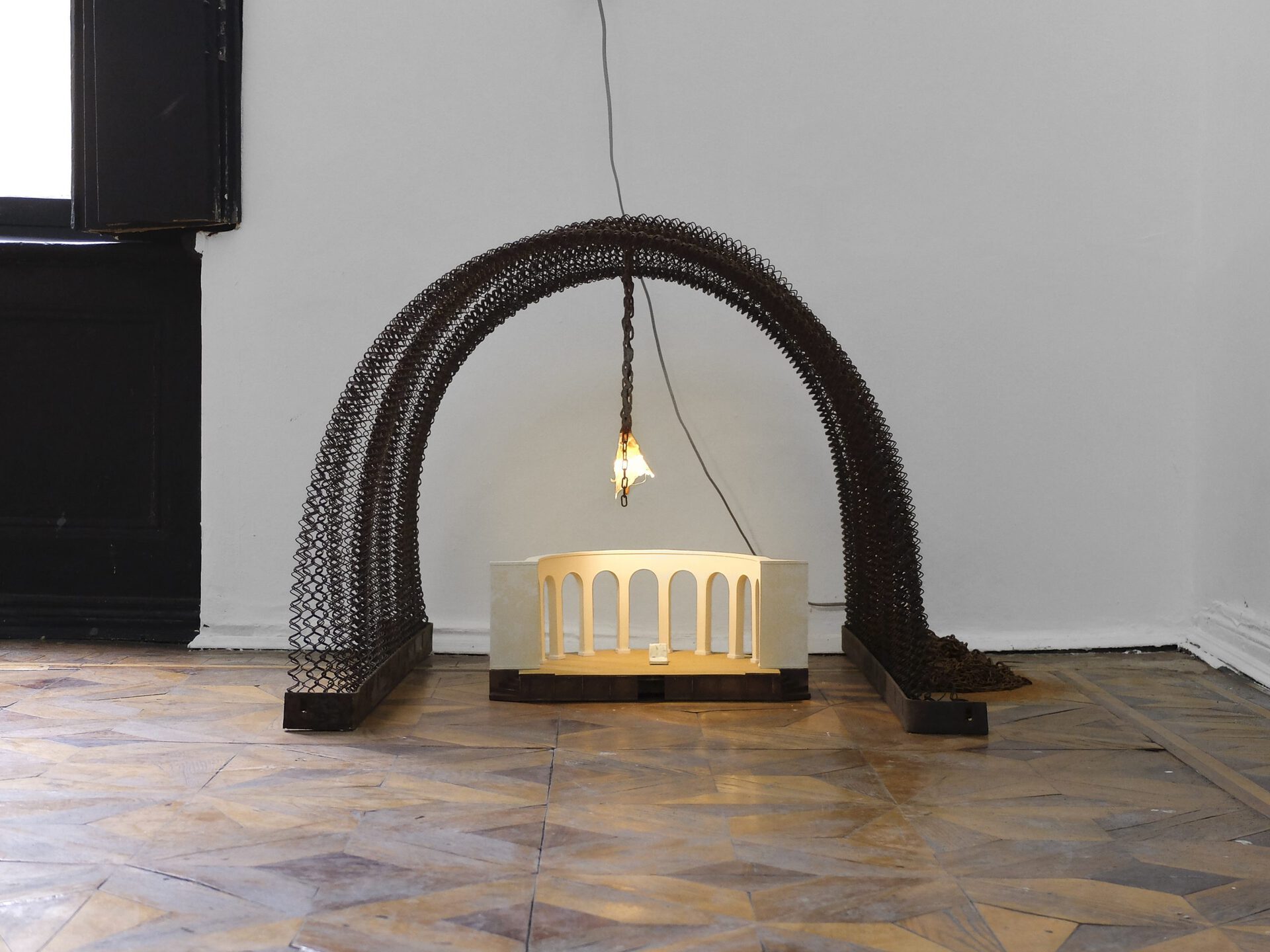 Sophie Jung, echo of the kennel b arch in spring (no man’s ouverture), 2021. arched bed spring, dog chain, wallpaper from abandoned rooms in a sanatorium, maquette of an abandoned stage and its back supporting character with main lead unleashed (back), 64 x 82 x 85,5 cm.