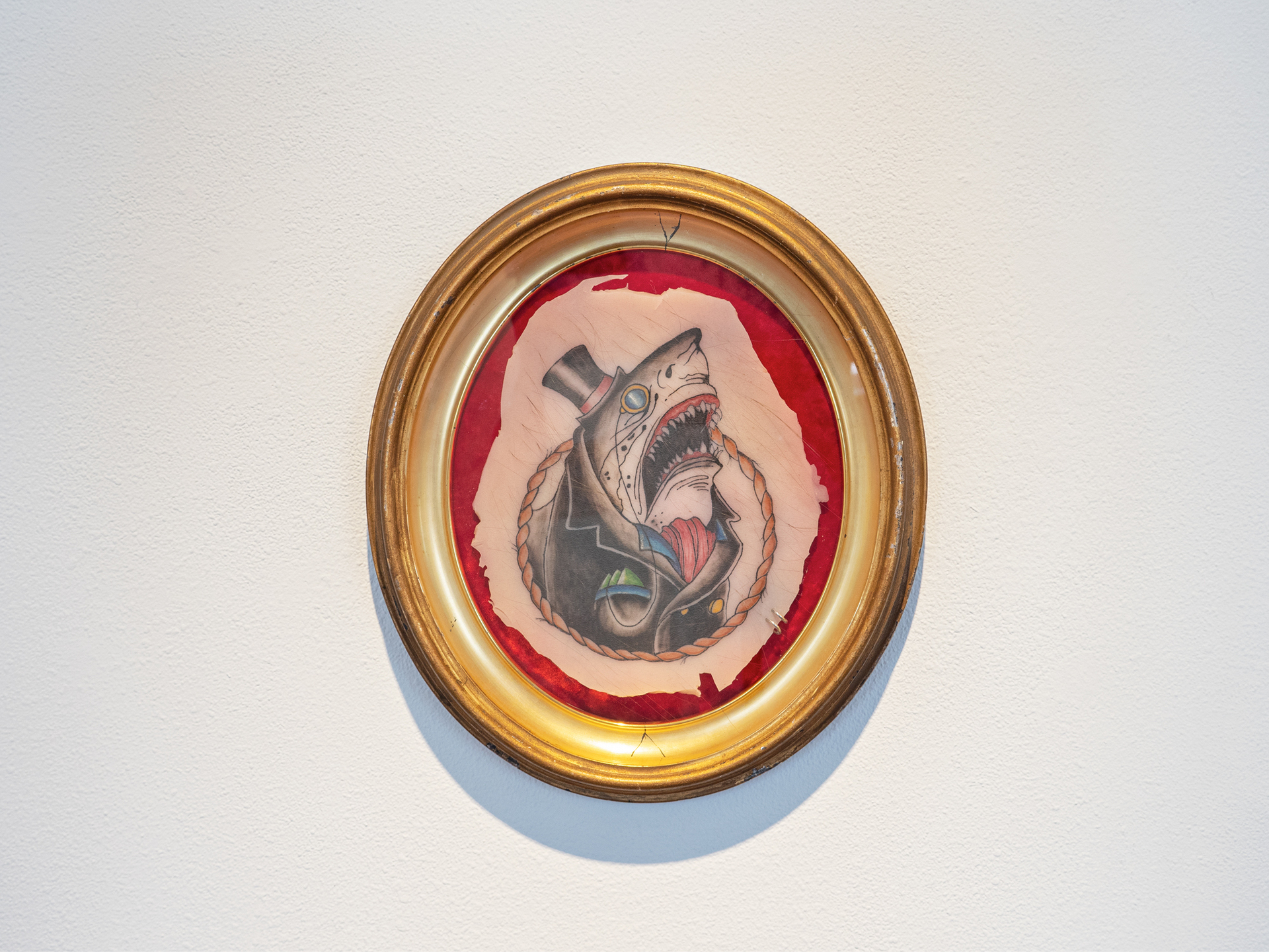 Portrait of A.R. (Mascot for the Creation of the Modern World, or, a troublesome irony over my concerns of theft considering the history of settler colonialism, or, The Middle Passage: Slave Ships & Shark Migration Patterns), 2021; Tattoo on silicone rubber, synthetic hair, piercing rings, vintage colonial era frame; 15 ½ x 13 ½ inches