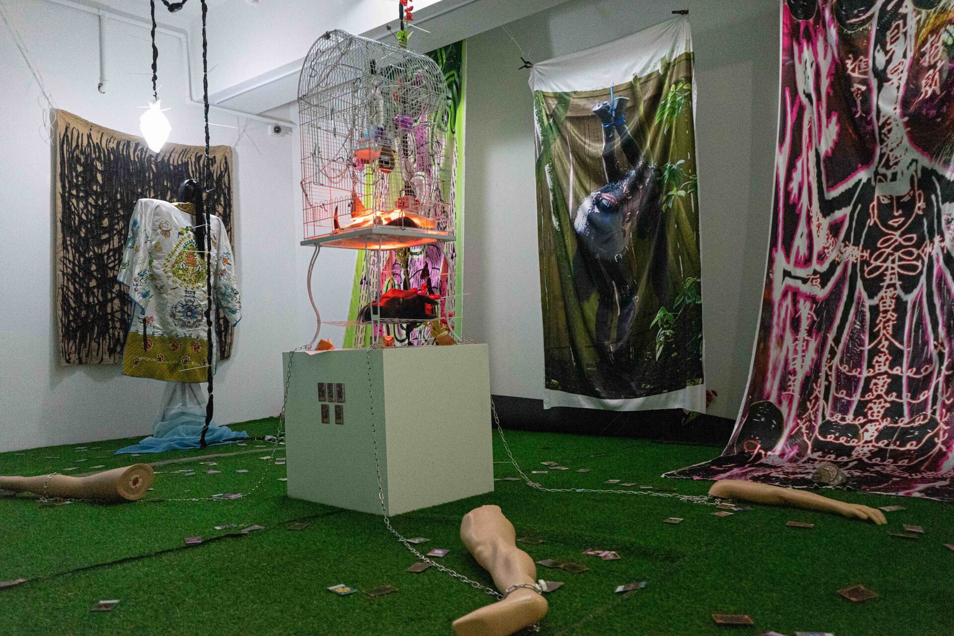 Chen Pin Tao, Equine (Mutilated), 2021, Stainless steel chains, birdcages, resin, latex mask, taxidermized bird, acrylic glass, figurines, cow skull, fluorescent light, taxidermized moths, jello powder, digital print on faux silk, horse hooves, yu-gi-oh cards, artificial bird nests, horse dildo, mannequin, dimensions variable