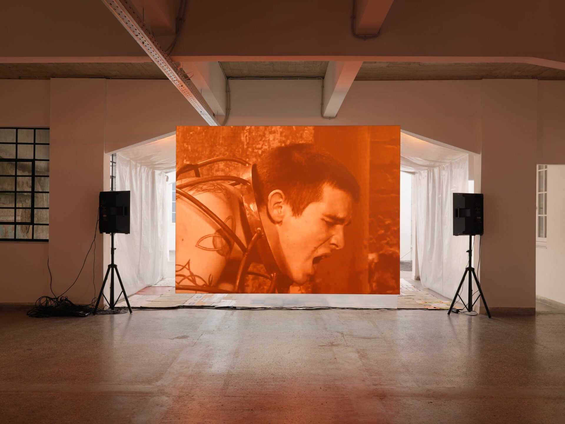 Foreground: Christian Friedrich, Untitled, 2010-11, SD video, color, silent, continuous play, 15 minutes, 22 seconds. Background: Aaron Ratajczyk, Remote Ressemblances, 2021, Cardboard packing boxes, contact mics, mixer, speakers + Aaron Ratajczyk, Home Ressemblances, 2021, Polyethylene sheets, metal strings and hooks