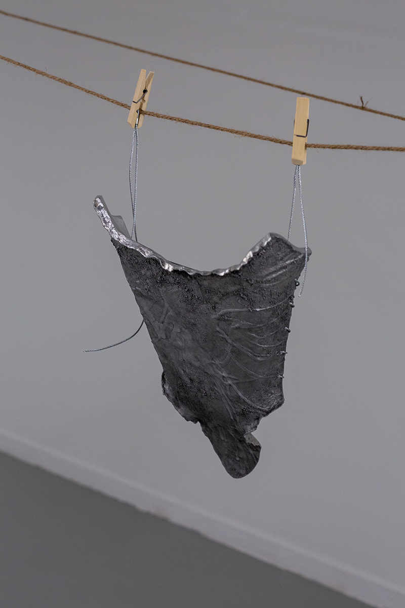 Self-portrait by Man Yau: Cast aluminum, wire, clothes peg, 50 cm x 28 cm x 10 cm, 2022.