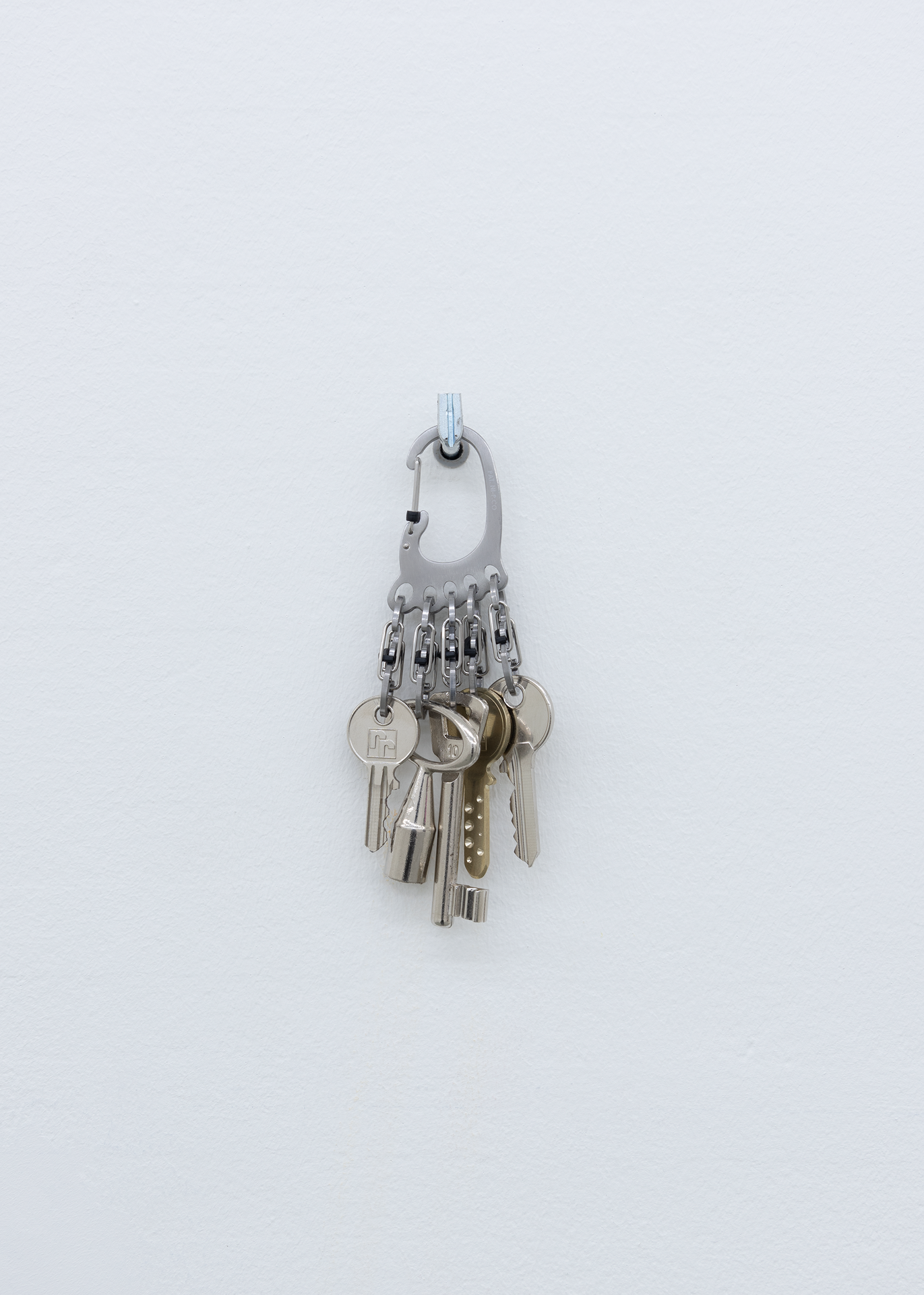 Wisrah Villefort. Keys, 2021. Various metals. Score: The keys of every door lock of the exhibition space to be made available to the artist. A copy of each of them to be displayed on a stainless keychain as specified by the artist. Exhibition duration.