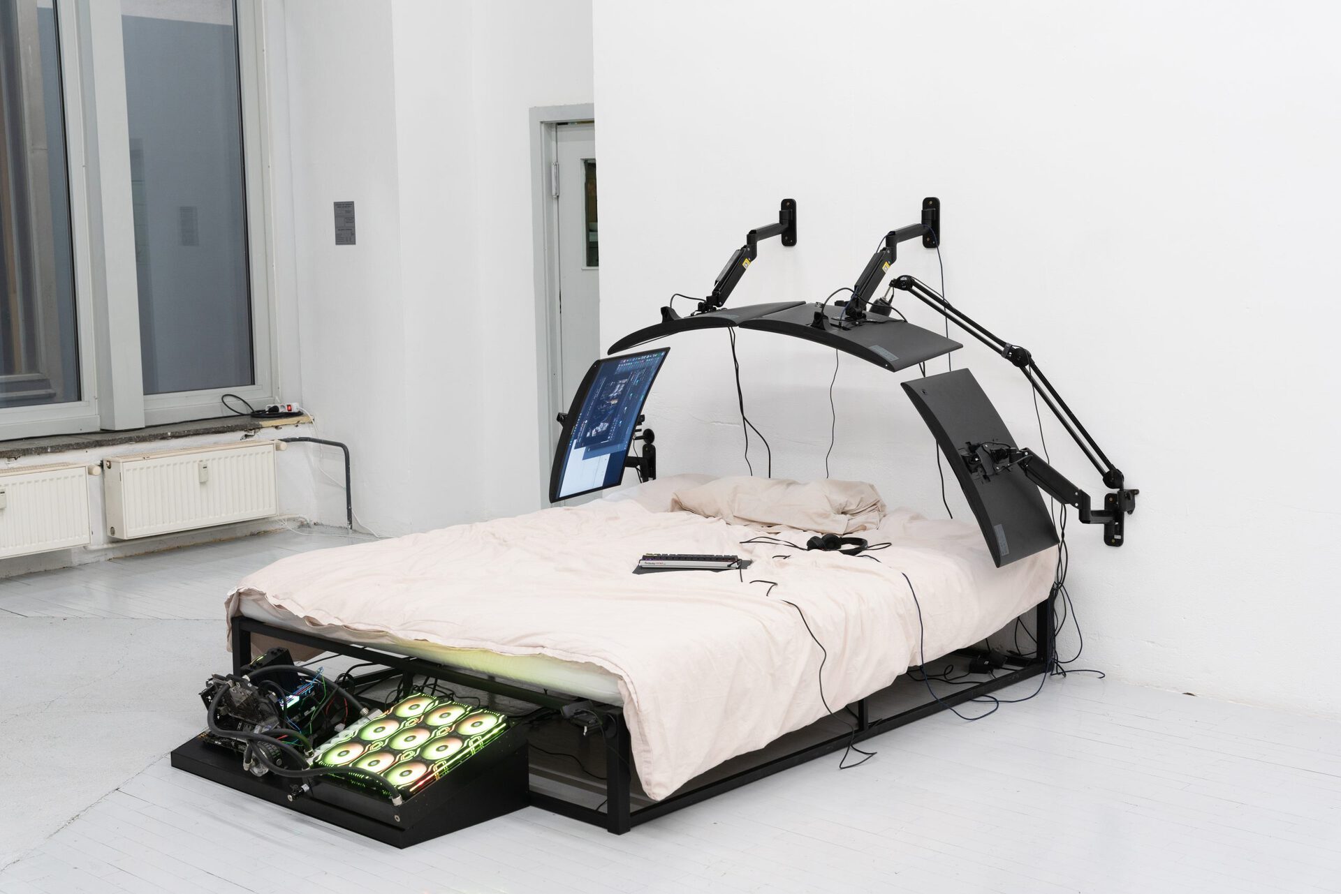 Filip Kostic, Bed PC, 2021, Custom built water cooled computer built into the frame of a bed, bed size variable, 4 curved monitors, cables mounted to wall, keyboard, streaming microphone mounted to wall, webcams, gaming mouse, peripheral computer