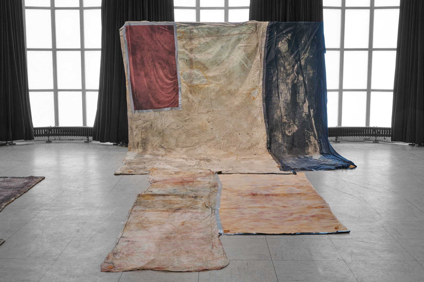 Dala Nasser: Red in Tooth, 2020 – 2021 – 2022. Discarded fabric, buried underground for 2 weeks to 3 months, ash, charcoal, rainwater. Kölnischer Kunstverein, 2022. Courtesy: the artist and Deborah Schamoni. Photo: Mareike Tocha.