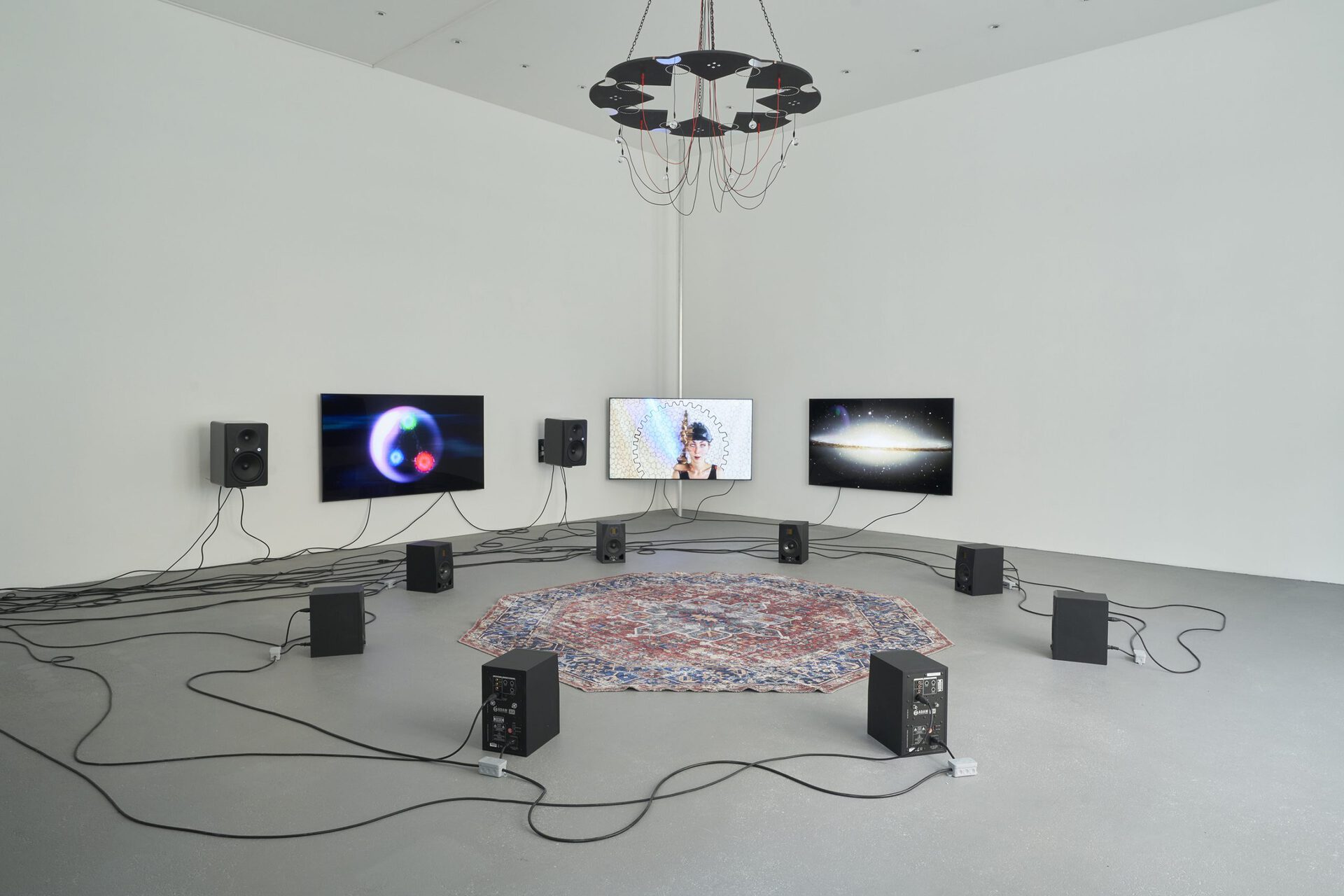 The Wave Epoch (Shamanic DMT Ritual @CERN causes Demonic Portal to open creating novel coronavirus UFO), 2022, three channel video installation, circle of eight speakers, octagonal carpet, wave chandelier, dimensions variable Courtesy of max goelitz Copyright the artists Photo: Milena Wojhan
