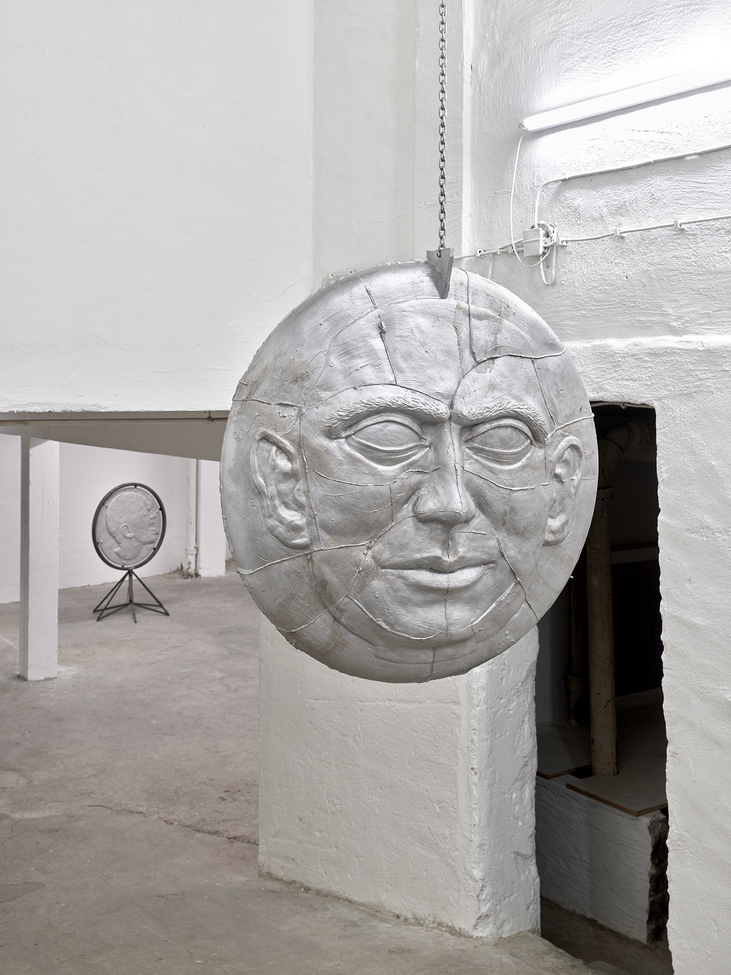 Lukas Schmenger, Portrait of the artist as the bell of the last round, 2022, cast aluminum, screws, chain, 92x92x13 cm, chain length variable