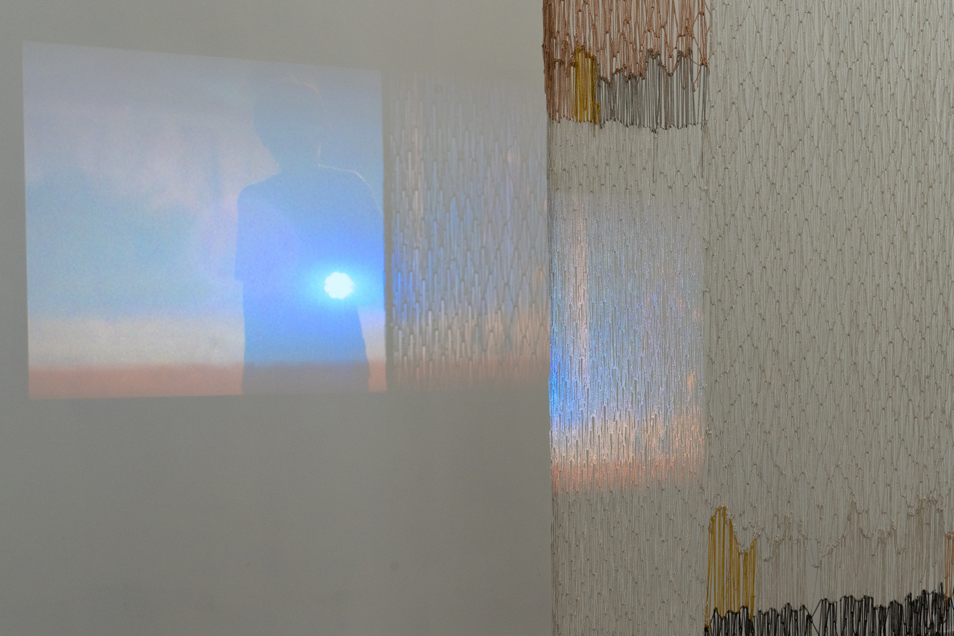 Elisa Florimond, projection “lights”, 2022 - ongoing series. video, 27 min and Maria Szakatz, “Untitled I”, 2022. Metal chains, 240 x 100 cm. Courtesy Rinomina and the Artists. Photo: Marcus Heim