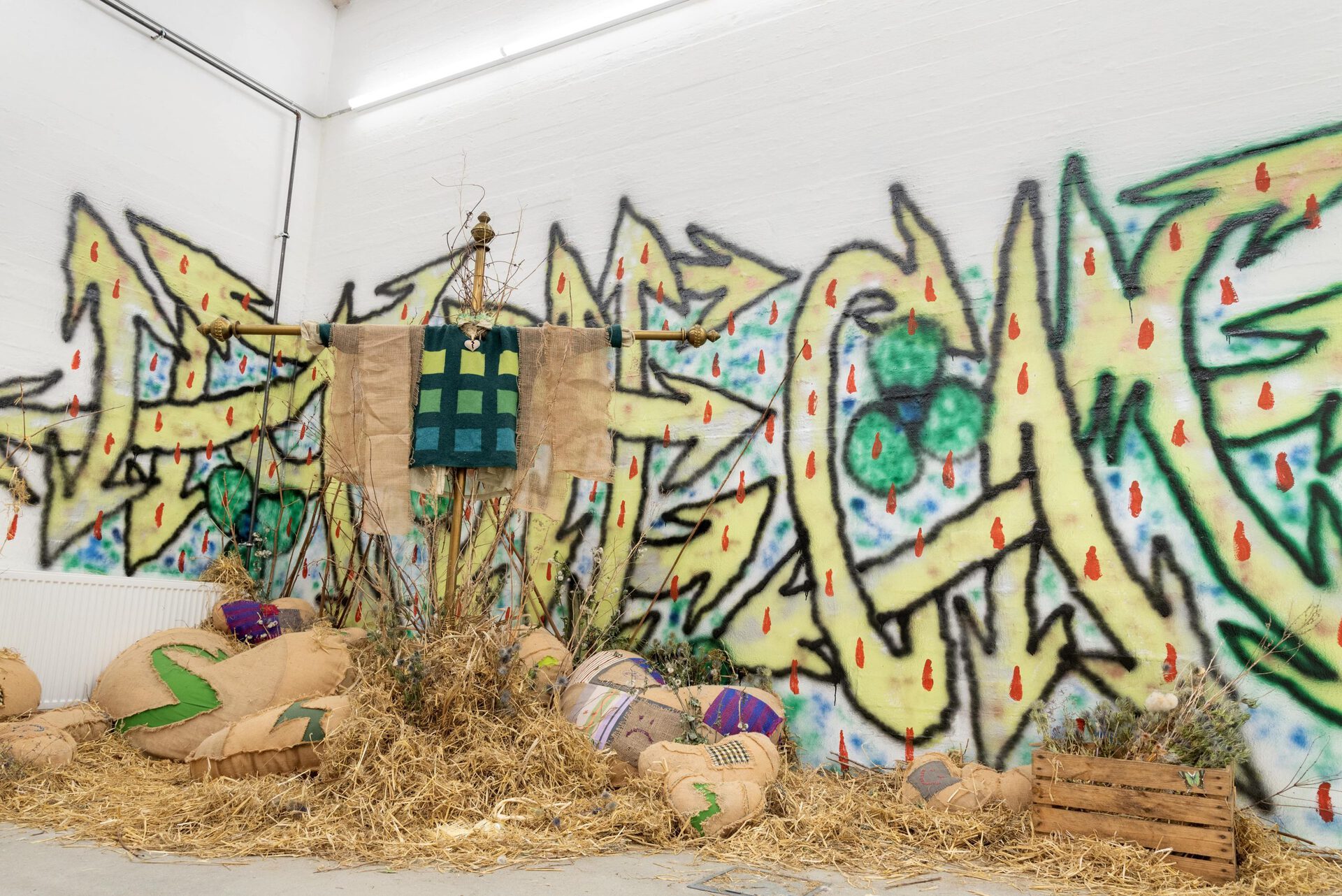 Olivia Rode Hvass, Hate The Game, 2022, Hessian, french curtain rods, heartbreak necklace, hay, roadside-plants, spray paint  (Heart-break pillows made in collaboration with seamstress Fredericke Kellberg – graffiti by anonymous painter)
