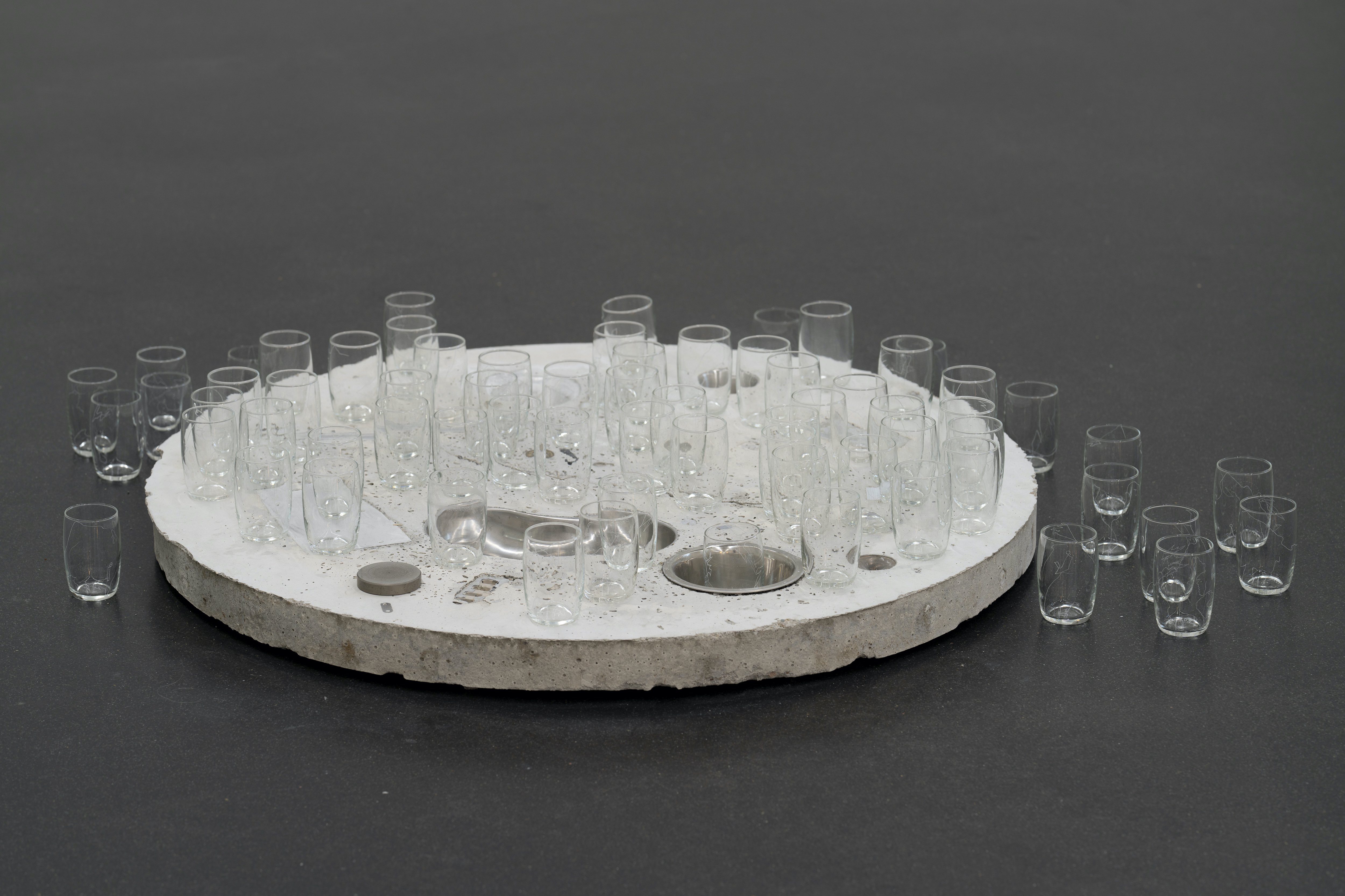 Table and Glasses (some of 250) 2022 Concrete, electrical scrap, found objects, engraved drinking glasses Width (table) 90 cm
