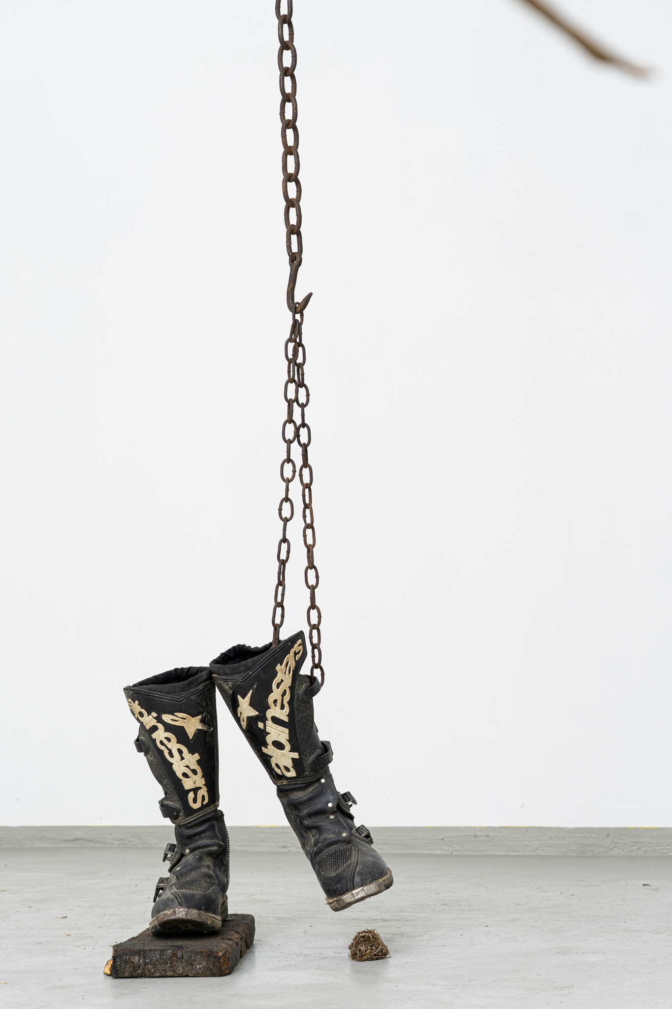 René Stiegler, Kick Start, 2022, 280 x 40 x 42 cm, Boots, Wood, Hay, Resin, Steel Chain, Steel Wire