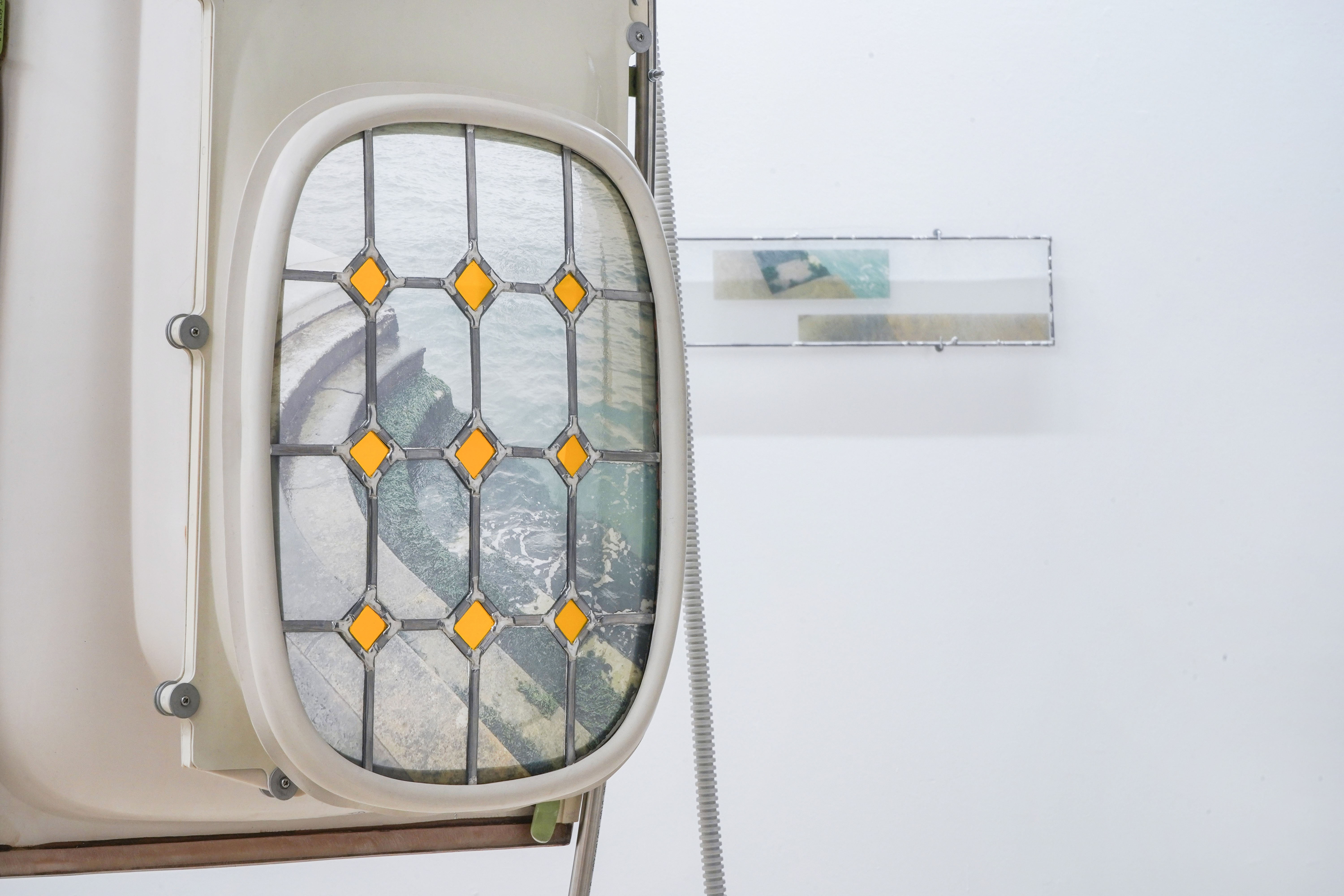 I’m standing on the Edge of the Land (2022). Airplane-window, Stained Glass, Metal, Light system. 200x80x75 cm 
