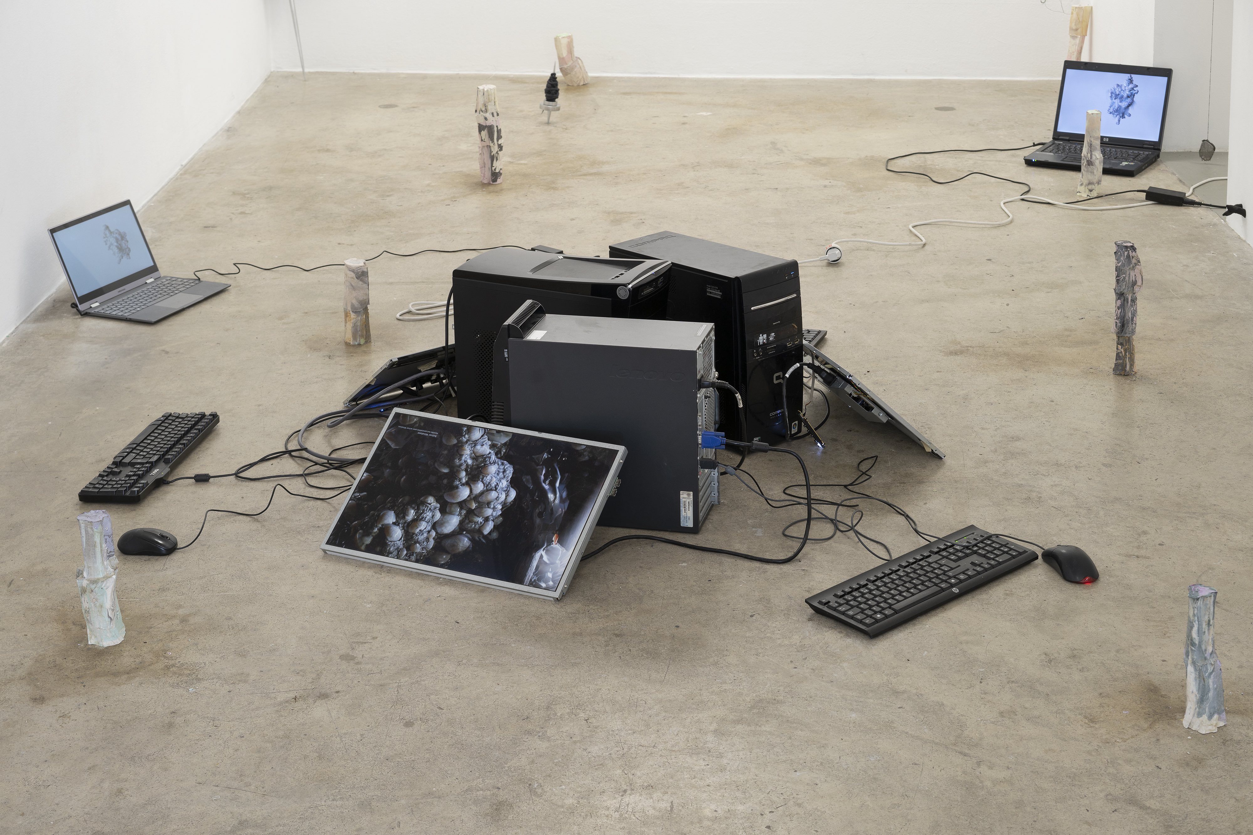 Installation View, center: Schwarm by Joerg Hurschler, 8 digital animations running on 5 laptops, 3 computer towers, 3 screens, 3 keyboards, 3 mice, various cables, 2023 left/right:  just do it by gousgous, cement, pigments, wire, various sizes, 2023
