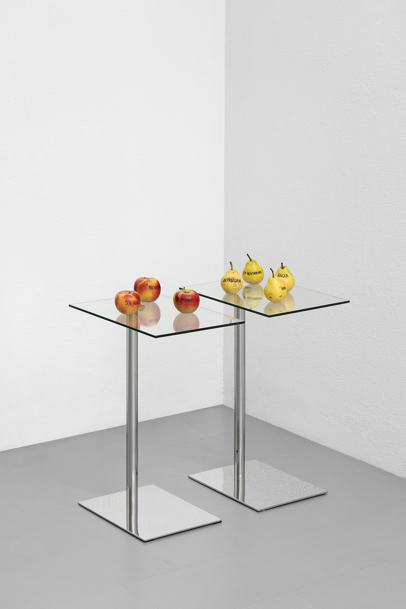 Paolo Bufalini, Self-doubt, Sex-addiction, Anorexia. Glass and steel table, tattooed Kanzi apples, 75x34x50cm; Anger, Ex-boyfriend, Depression, Paranoia, 2023. Glass and steel table, tattooed Kaiser pears, 75x34x50cm. Courtesy of the Artist and La Rada. 