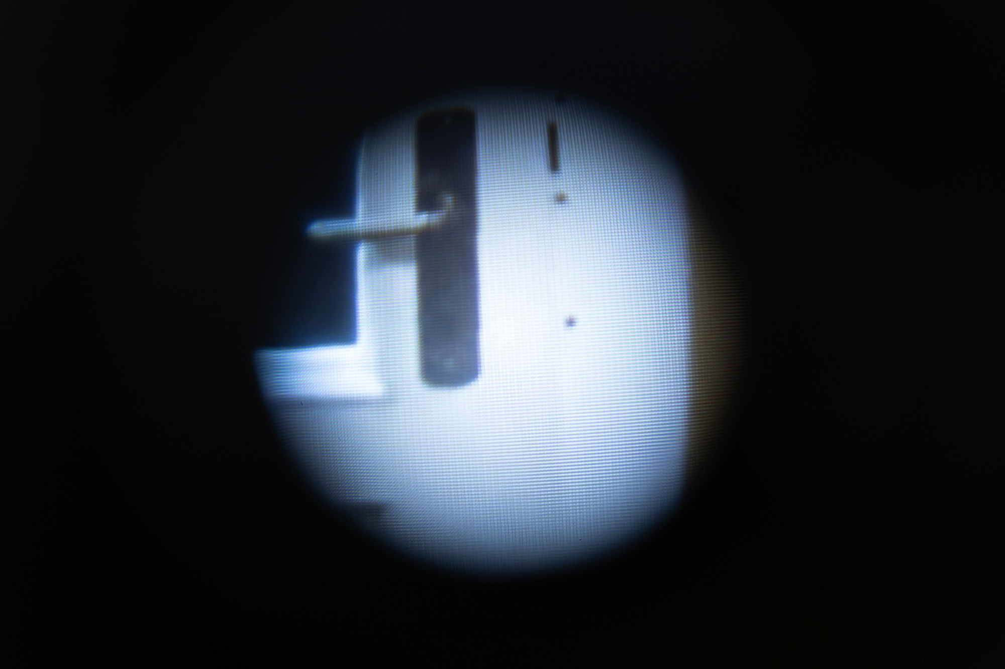 Ian Waelder. You Who Are The Stranger (Moth Joke), 2023. Door peephole on wall, muted video played on screen. 9 mins.
