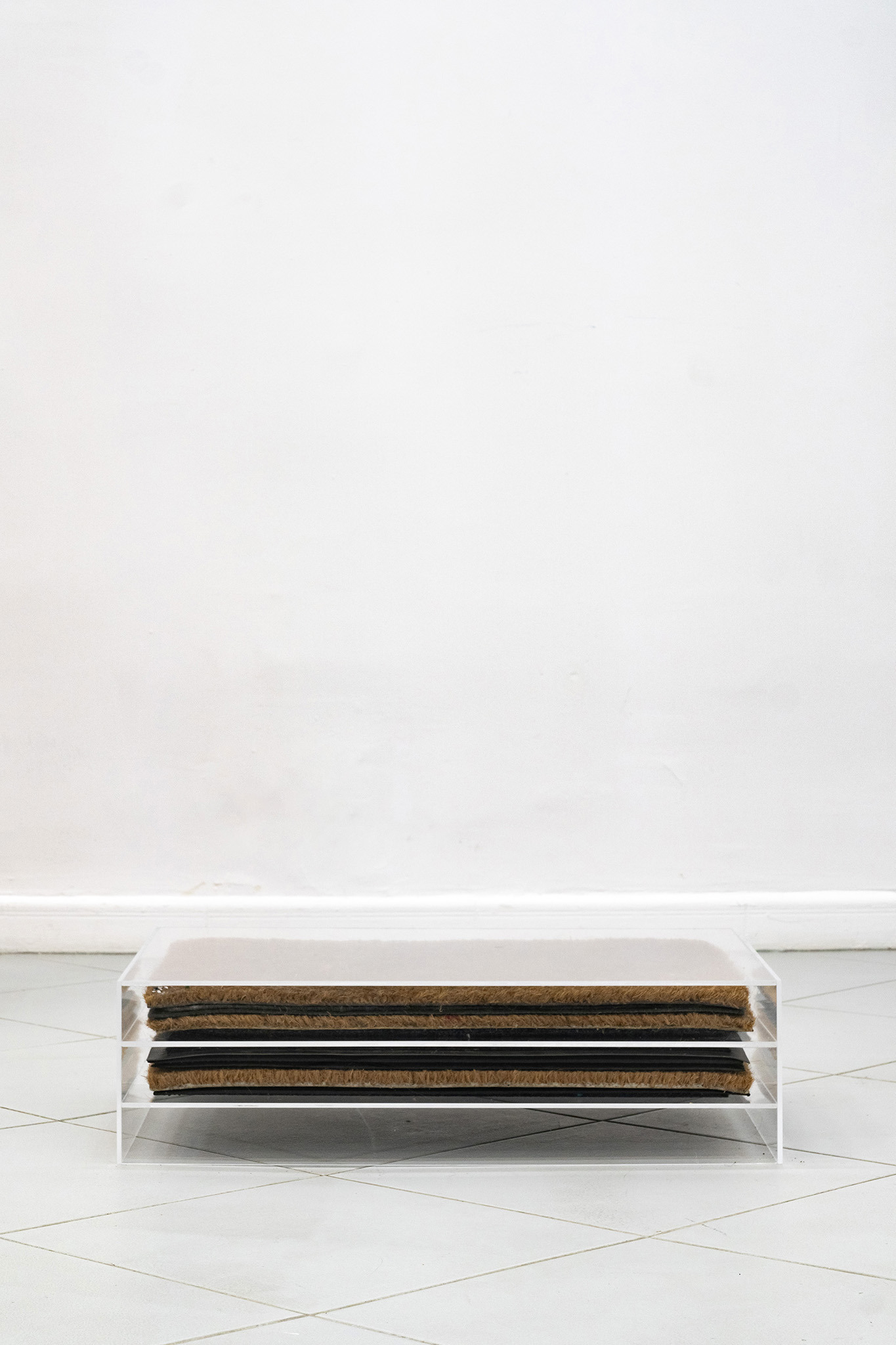 Jan Domicz, Neighbors’ doormats collected via exchange, 2024, plexiglass, doormats, 70 x 18 x 50 cm