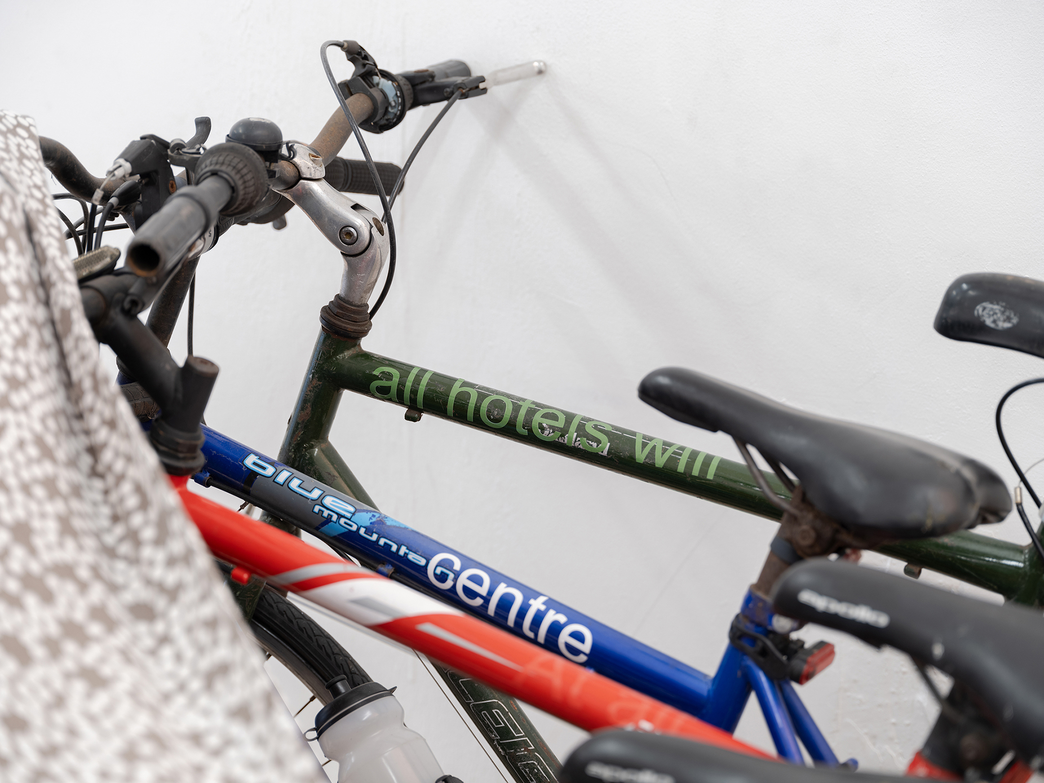 Sam Cottington, Me and all hotels will centre At all You had it Its image of him living appears (detail), 2024, bikes, mugs, bed sheet, vinyl text, sports bottle, dimensions variable. Photo: Eleonora Agostini