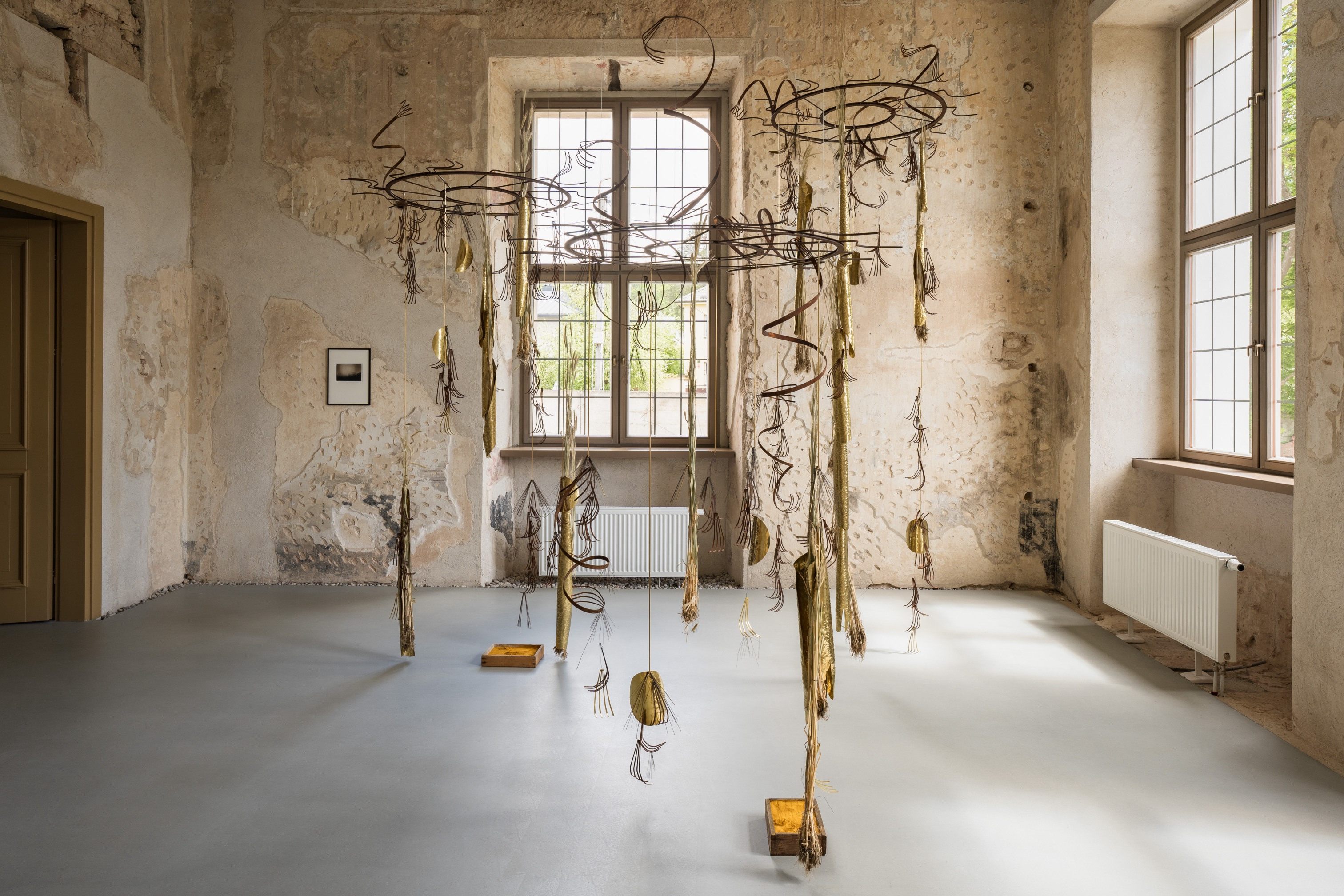 Iza Tarasewicz. Looped Processions IV, 2022. Oxidised steel, brass, wheat, wire in three segments. Dimensions variable; and Yellow Coal, 2016/2022. Ochre, wood. Dimensions variable. Photographer: Andrej Vasilenko