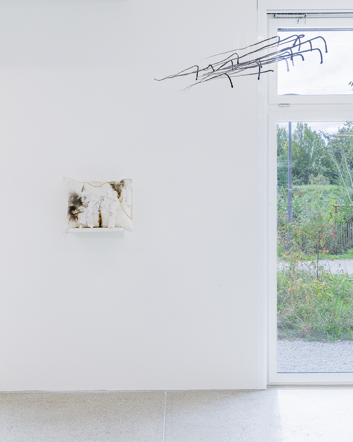 Exhibition view; Élie Autin, Pillow, 2023, hand-sewn cushion enhanced with sewn additions, 60 x 50cm; Arrow, arrows in synthetic hair dipped in resin, CALM - Centre d'Art La Meute, 2024/Photo: Théo Dufloo/Courtesy of the artist and CALM.