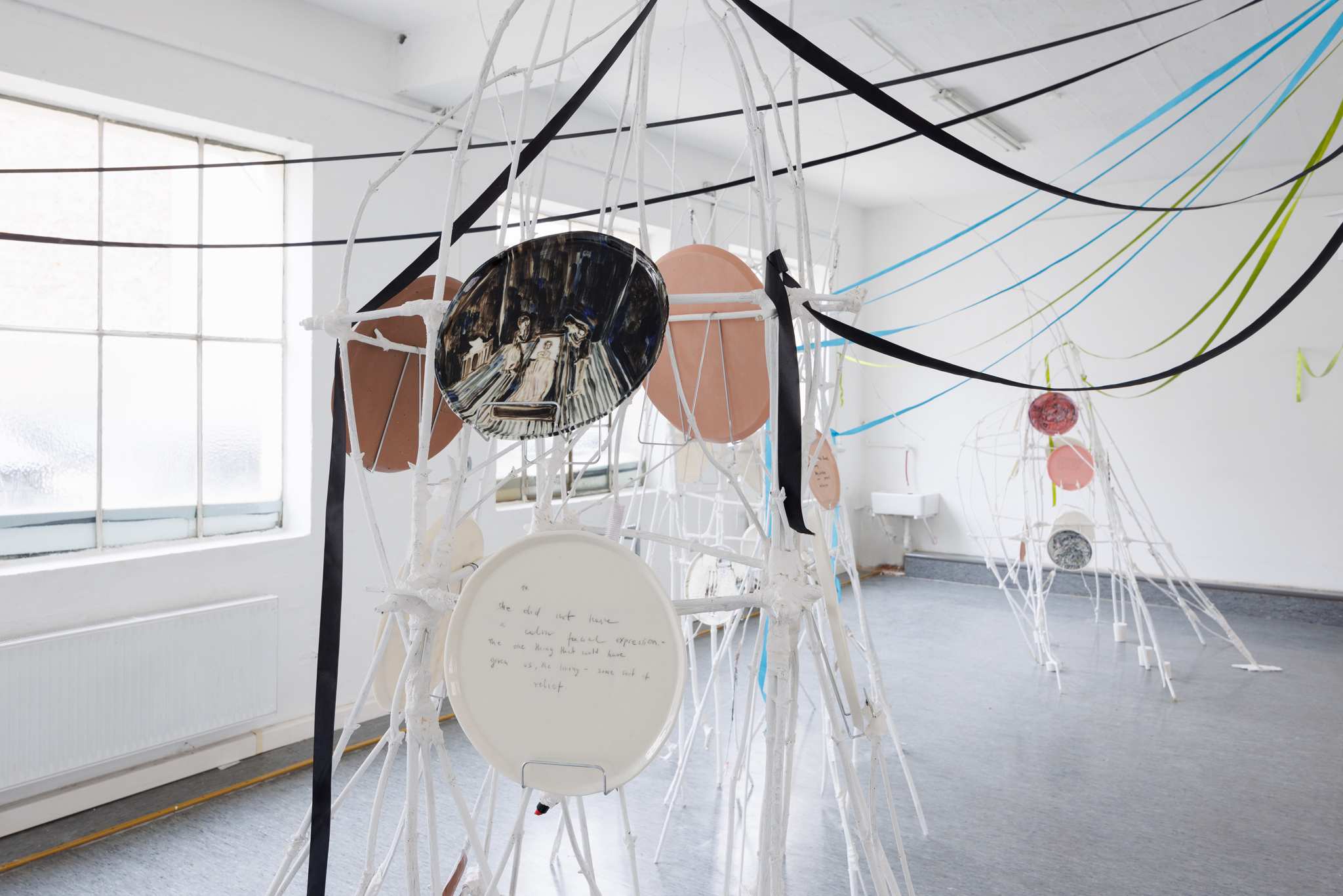 Anna Łuczak, Sophie Schmidt, “Brutality of Spring,” 2024, installation view (porcelain plates, white paint, wood ribbon, metal plate holders, cutlery, make up).