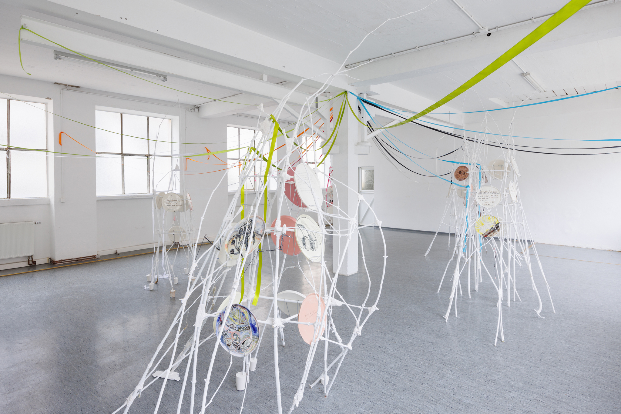 Anna Łuczak, Sophie Schmidt, “Brutality of Spring,” 2024, installation view (porcelain plates, white paint, wood ribbon, metal plate holders, cutlery, make up).