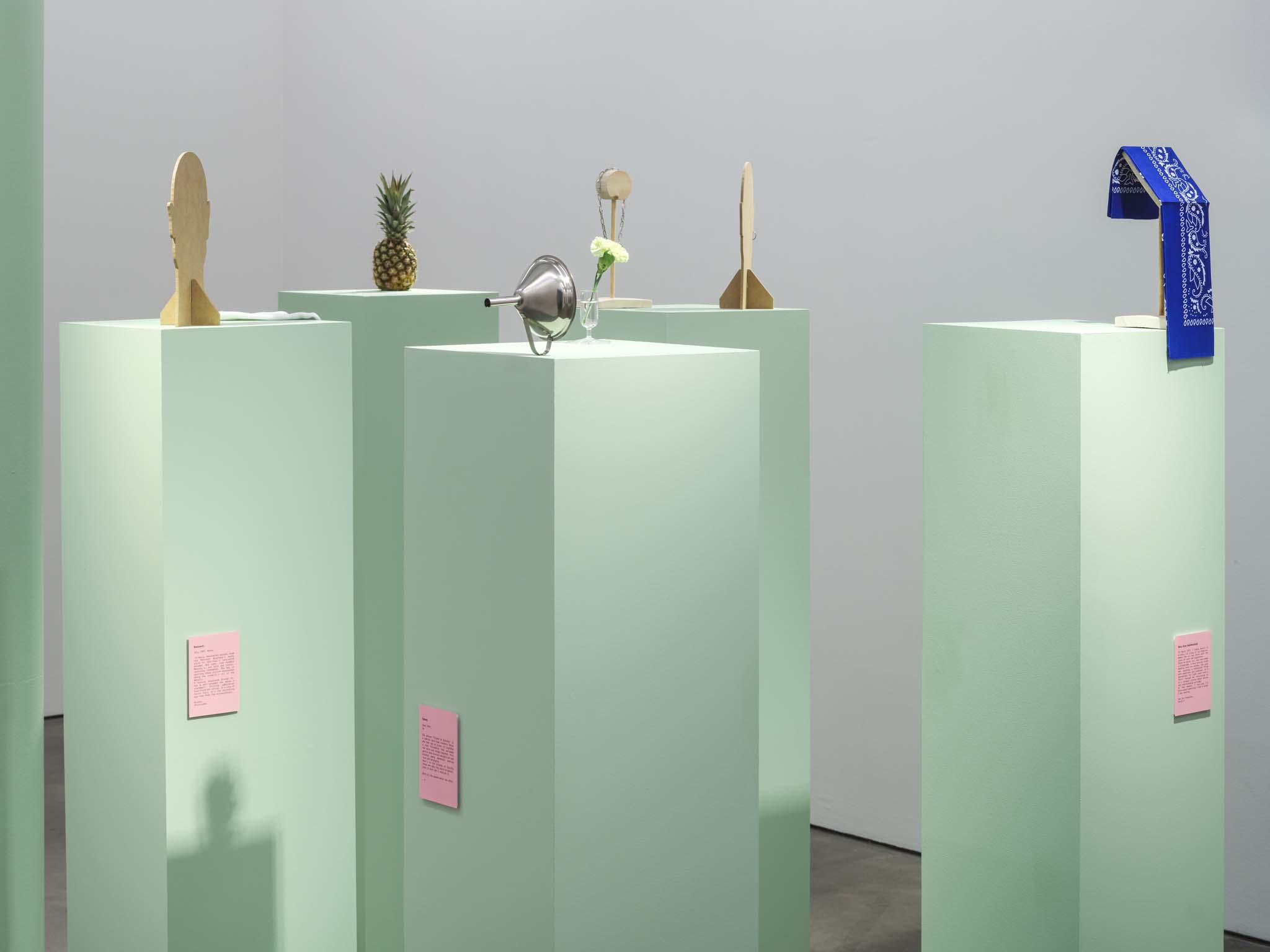 Other Dead Giveaways, 2024, Dimensions variable, Navy handkerchief, plaster pineapple, silver earring, faux mustache, green carnations, metal funnel, striped tube socks, Oscar Wilde green