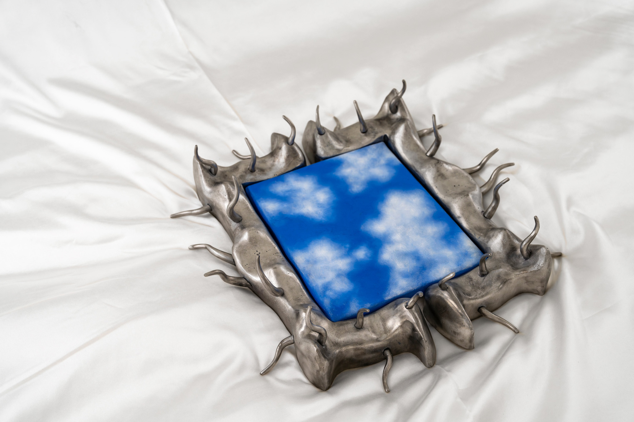 one morning, when he woke up from troubled dreams, he found himself on his bed transformed into a giant sky, 2024, steel, foam, aluminum casting, oil painting on canvas, satin duvet cover, MDF slide