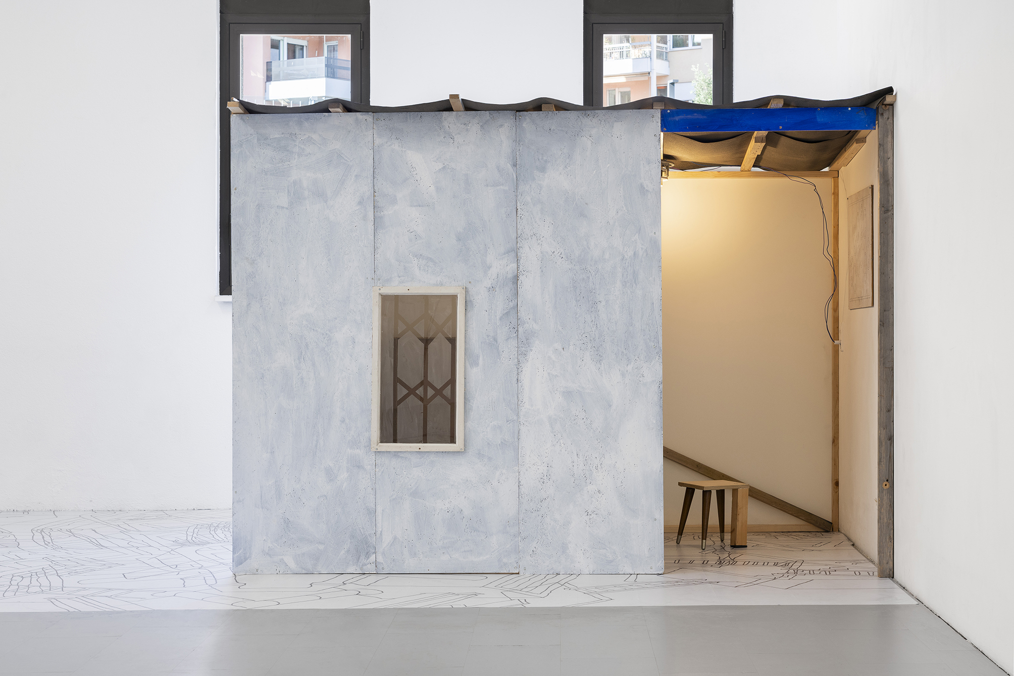 Aldo Mozzini, Quasi un rifugio, 2025. Drawing, large poster on poster paper, 356 x 504 cm – MDF panels, window made with yoghurt, bituminous paper, white wooden flag, stool, lamp, intaglio, printing fabrics, plastic waste, wood, 220 x 280 x 140 cm. 