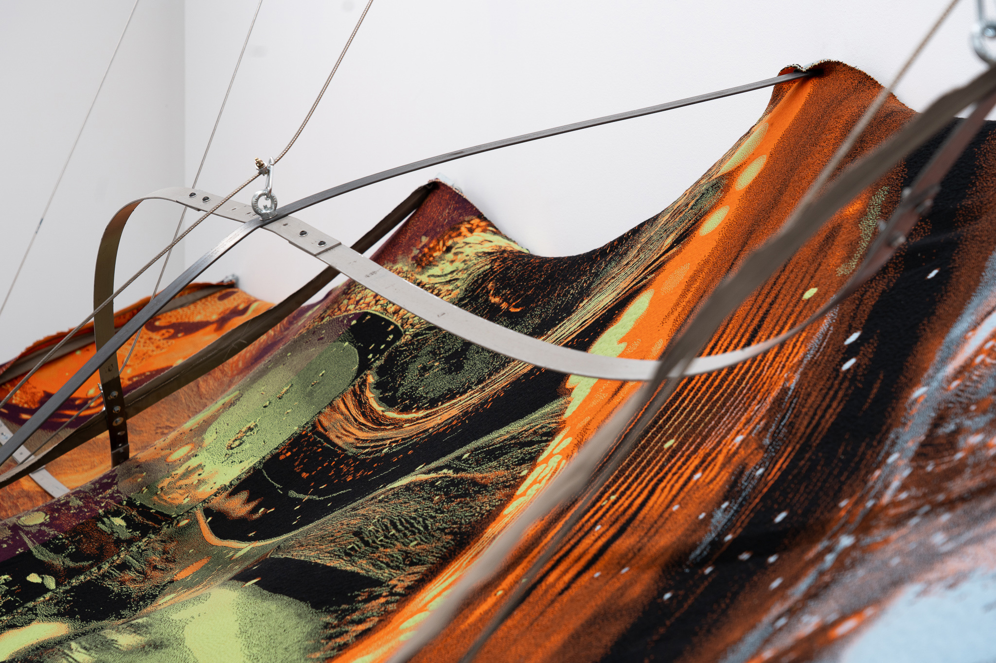 Nicola Arthen - Reading A Reflection (2025); Collage from generated images, machine-knitted wool, cotton and filling yarn, steel rig, C-prints, wooden carts with engravings, work pants, lights, sensors (760x160x145cm), courtesy of the artist and Platform