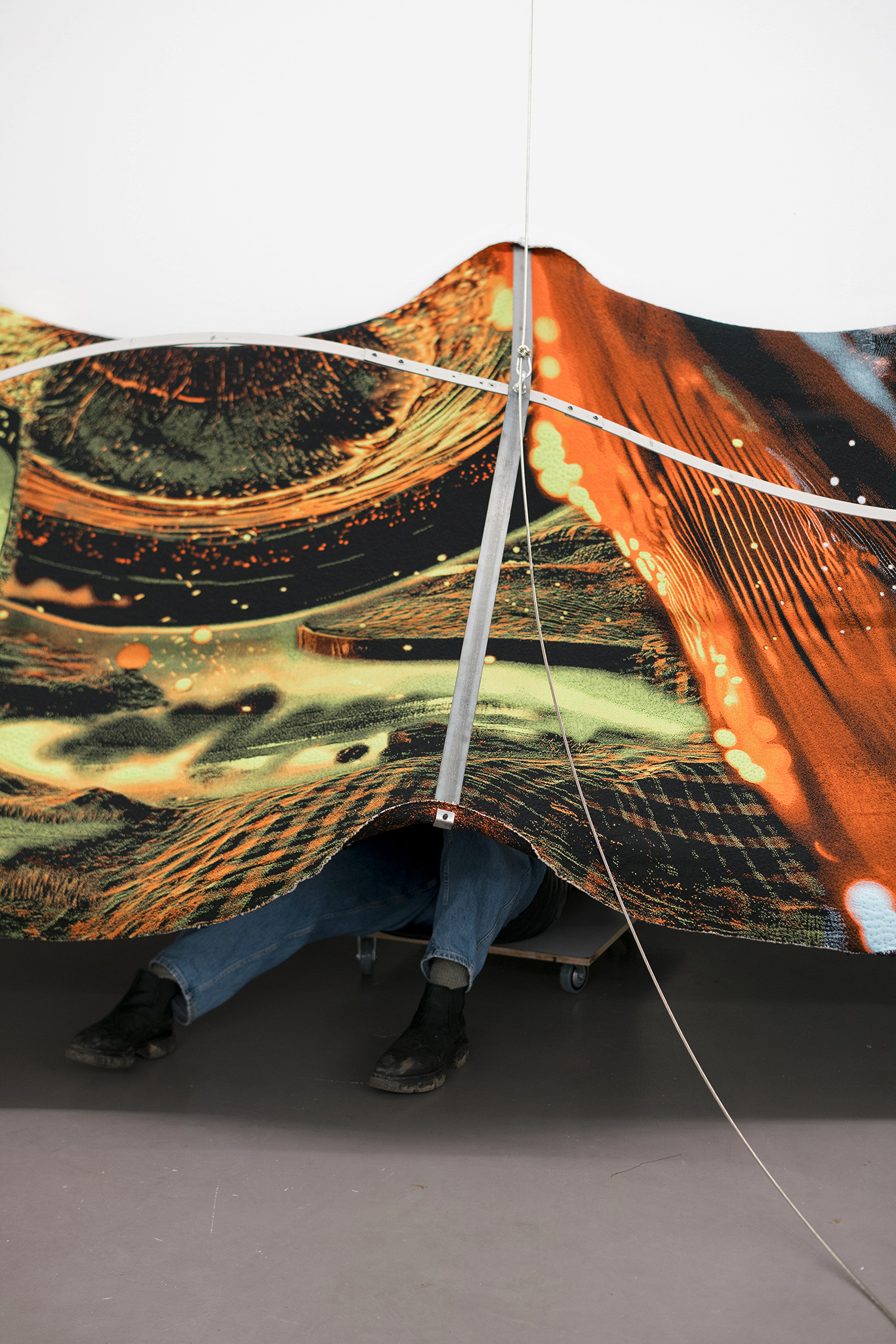 Nicola Arthen - Reading A Reflection (2025); Collage from generated images, machine-knitted wool, cotton and filling yarn, steel rig, C-prints, wooden carts with engravings, work pants, lights, sensors (760x160x145cm), courtesy of the artist and Platform