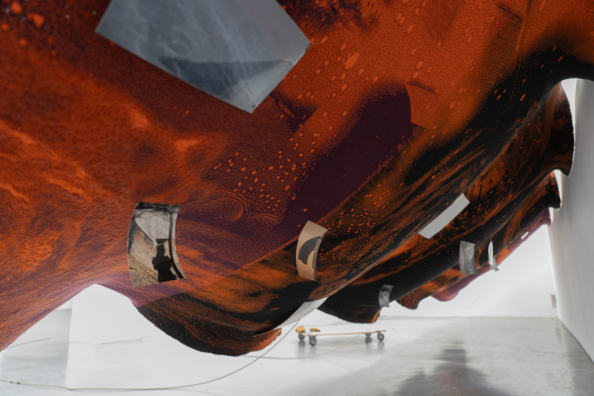 Nicola Arthen - Reading A Reflection (2025); Collage from generated images, machine-knitted wool, cotton and filling yarn, steel rig, C-prints, wooden carts with engravings, work pants, lights, sensors (760x160x145cm), courtesy of the artist and Platform