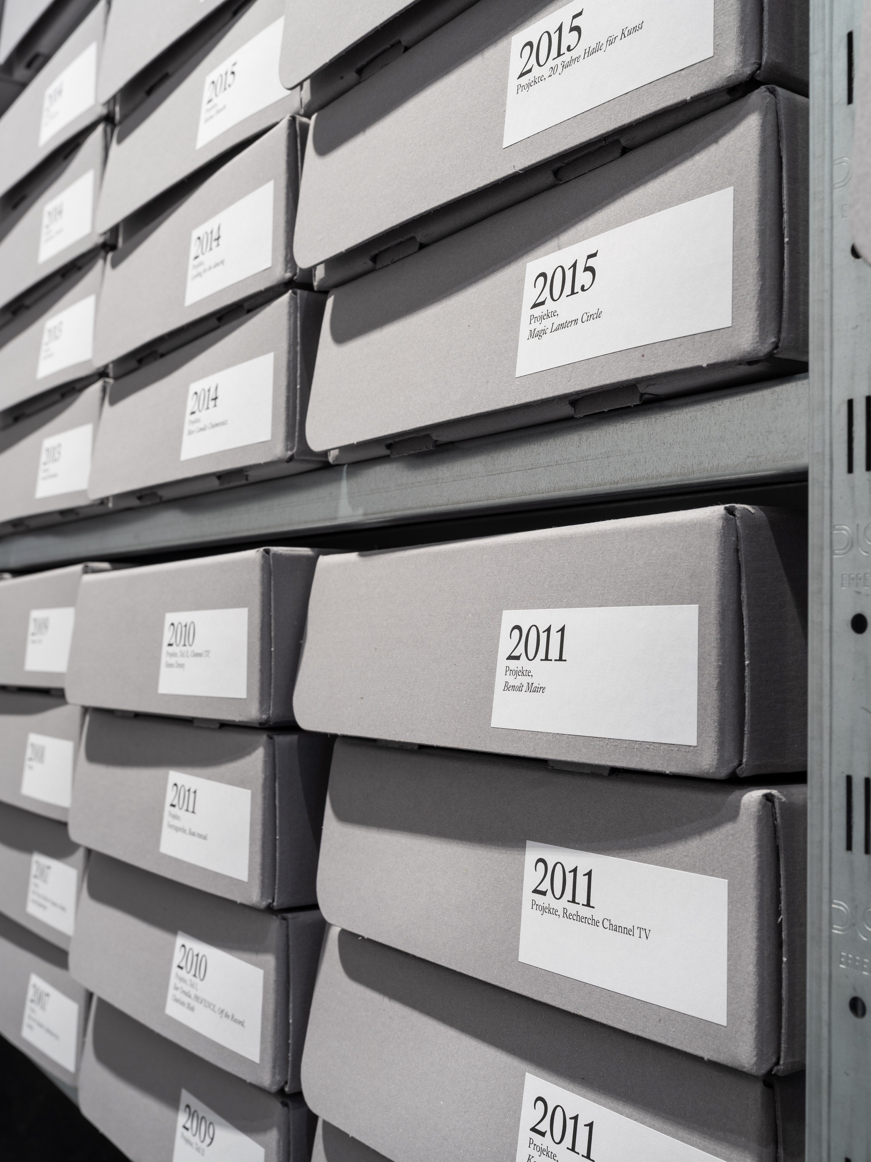 Archiv / Archive, Shelving system, lighting system, shelf ladder, wall paint, floor paint, archive boxes with adhesive labels, vinyl lettering, 350x113x391cm, 2025, Photography: Fred Dott