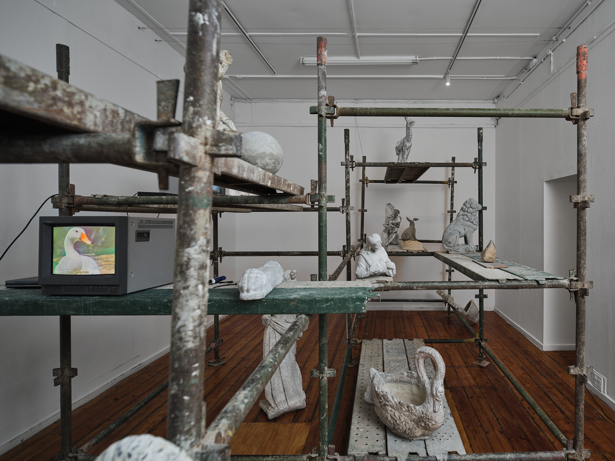Installation View of the "Cast Room" including 15 cement garden ornaments (Ruined by the act of copying metal over their forms) 2 video works with audio and construction scaffolding (exhibited in near darkness)