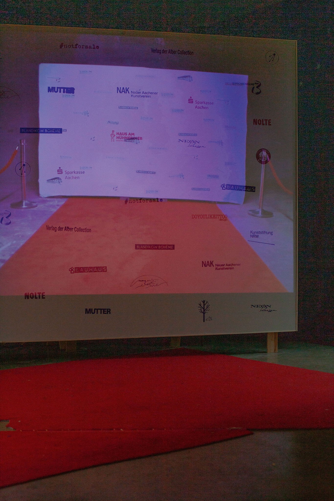 Béla Pablo Janssen, Installationsansicht Logowand Theater der Sonnenzuwendung, 2026, Detail, Roter Teppich Blandikow, 2020-2026, Filmstills, Roter Teppich Blandikow, 2020-2026, Erdgeschoss.