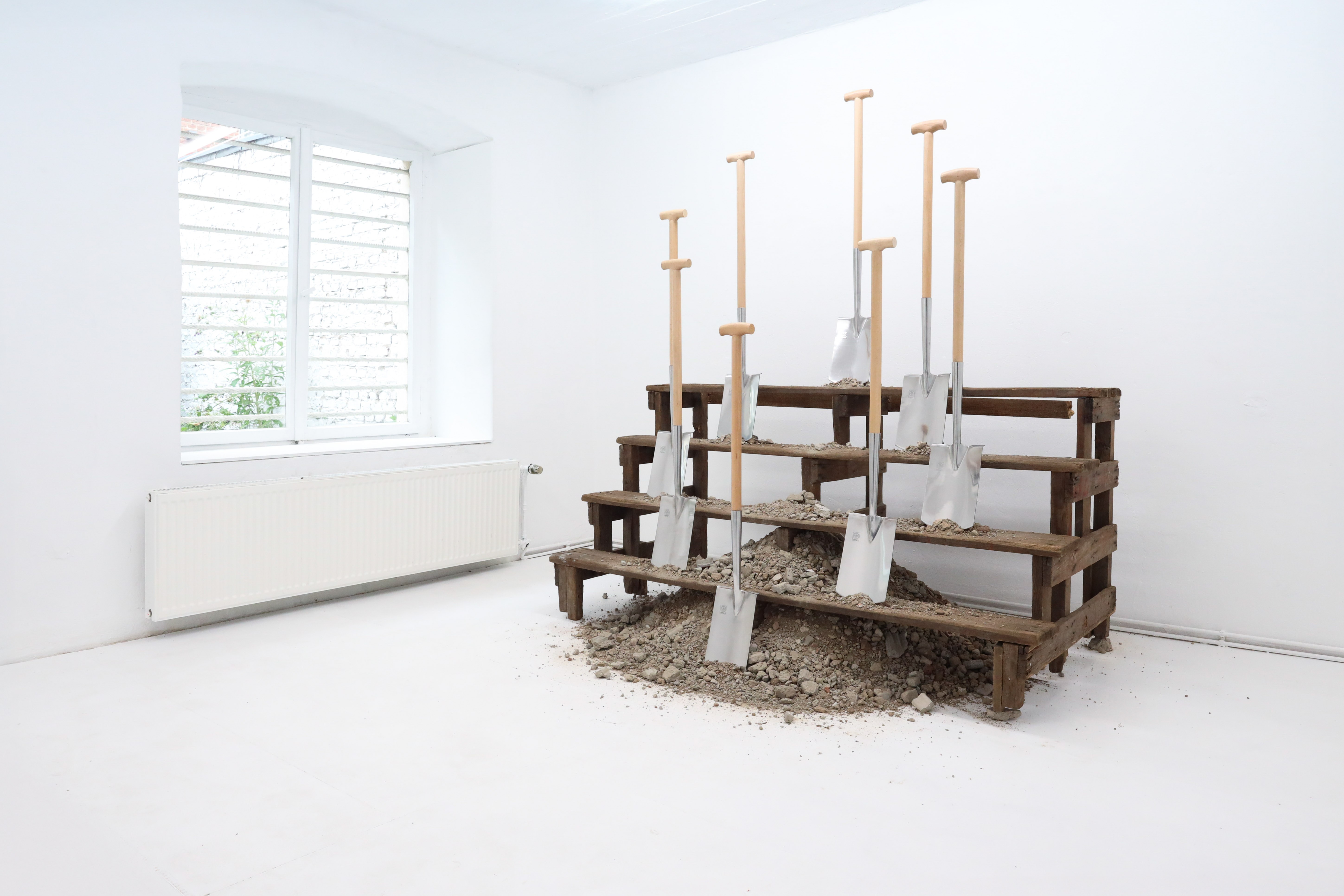 Installation view of 'Angehörige', 2026, wooden stairs, eight spades, concrete recycling, 200 x 117 x 213 cm, by Mathias Weinfurter, DOD Gallery, Cologne, 2026